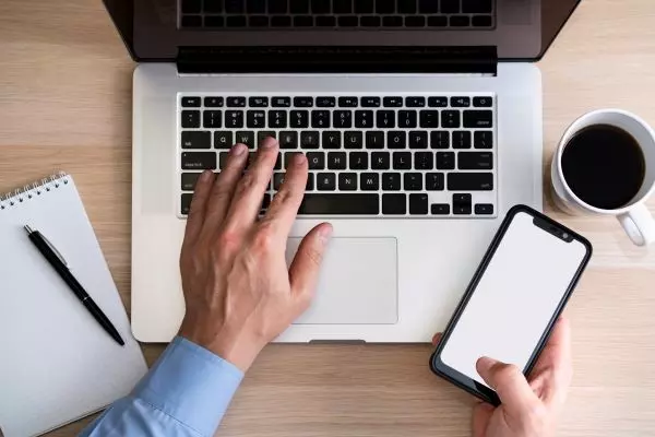 homme qui tape sur clavier ordi avec téléphone portable en mains